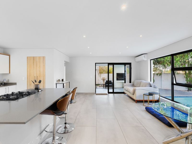 Modern open-plan living area featuring a sleek kitchen with a central island, gas cooktop, and seamless flow to the outdoor patio through sliding doors.