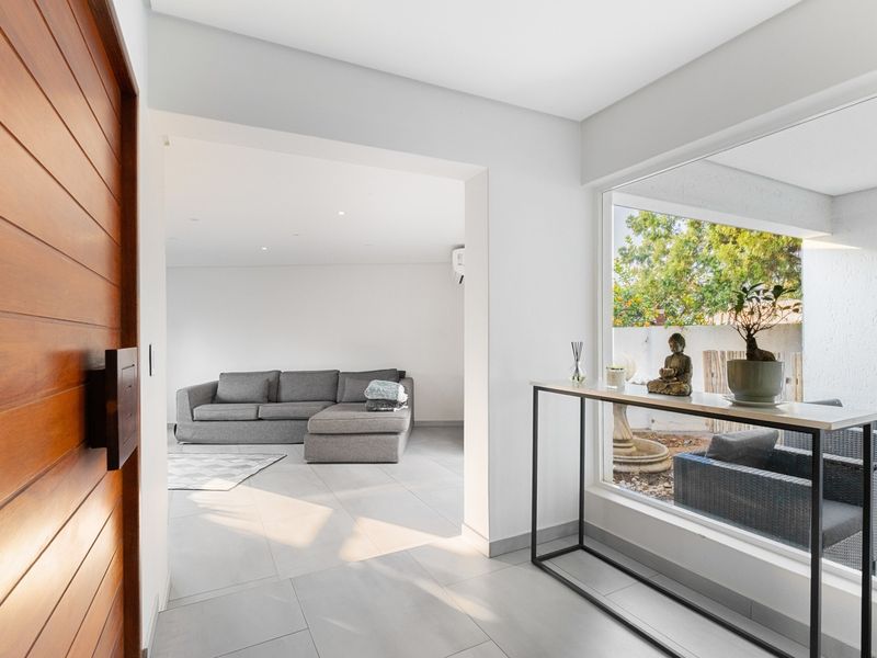 Bright and modern entrance hall featuring a solid timber door, large picture window overlooking the garden, and neutral tiled flooring.