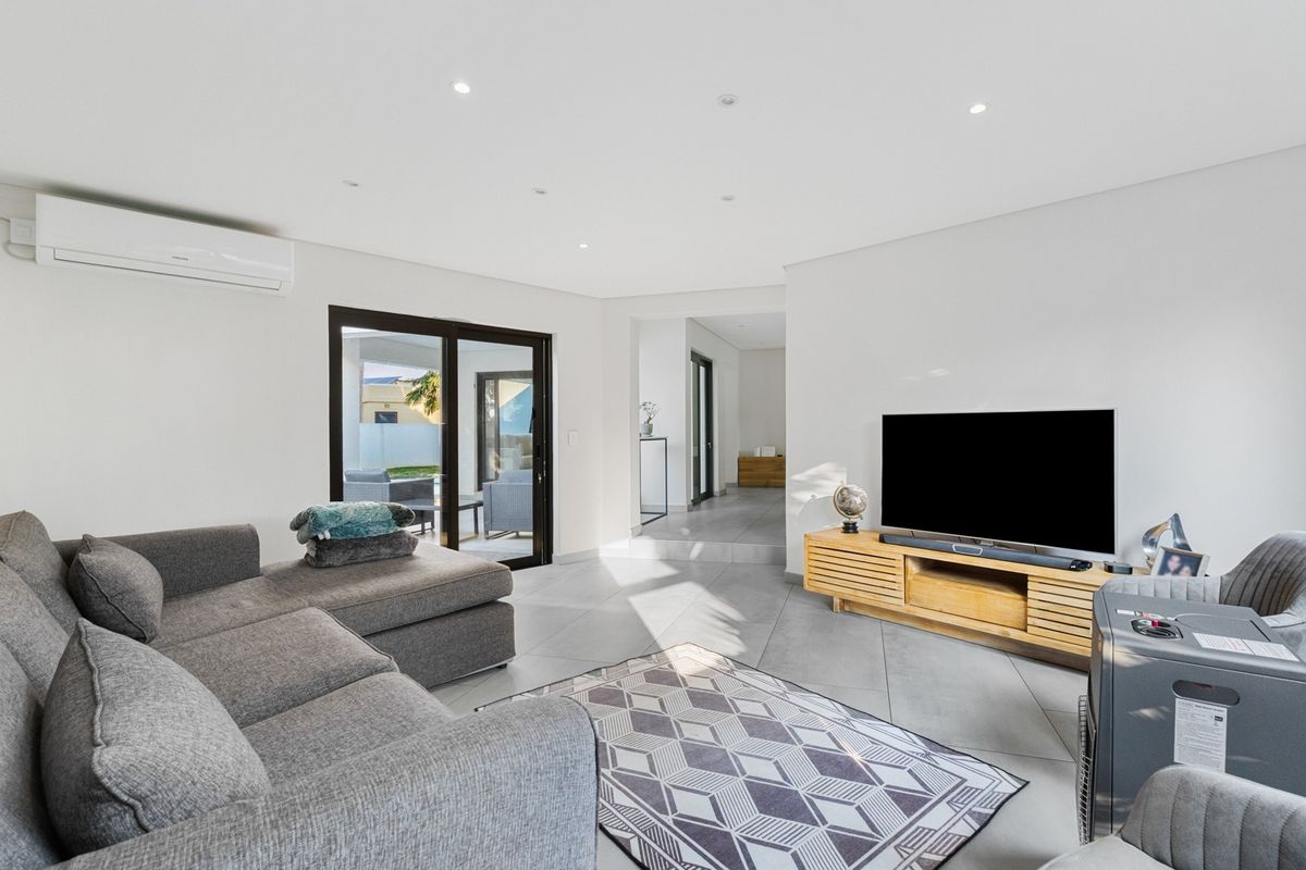 A bright, modern living room featuring tiled flooring, recessed downlighting, a wall-mounted air conditioning unit, and sliding glass doors leading to an outdoor area.
