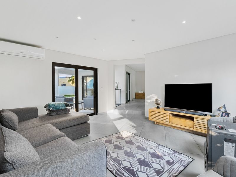 A bright, modern living room featuring tiled flooring, recessed downlighting, a wall-mounted air conditioning unit, and sliding glass doors leading to an outdoor area.
