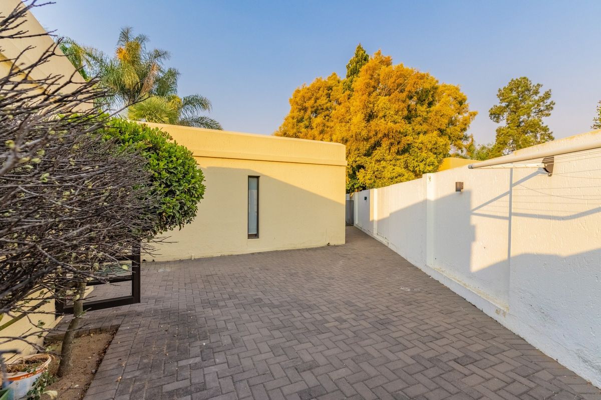 A clean, paved rear courtyard area featuring a boundary wall, wall-mounted lighting, and a fixed clothesline.
