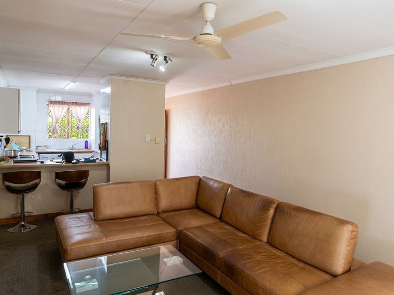 Open-plan living area featuring a breakfast bar kitchen, ceiling fan, and neutral wall finishes, offering a functional layout for modern apartment living.