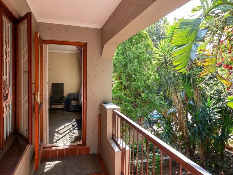 A covered balcony featuring tiled flooring and a metal balustrade, providing an outdoor transition space with views of the surrounding garden.