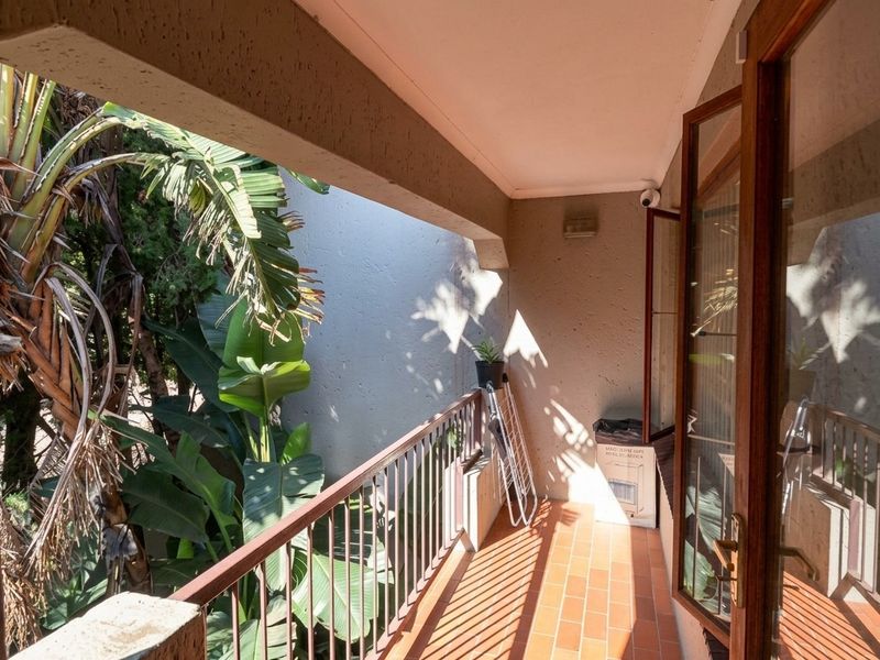 A private balcony featuring terracotta tiling, a metal balustrade, and direct access through timber-framed glass doors, overlooking lush garden greenery.