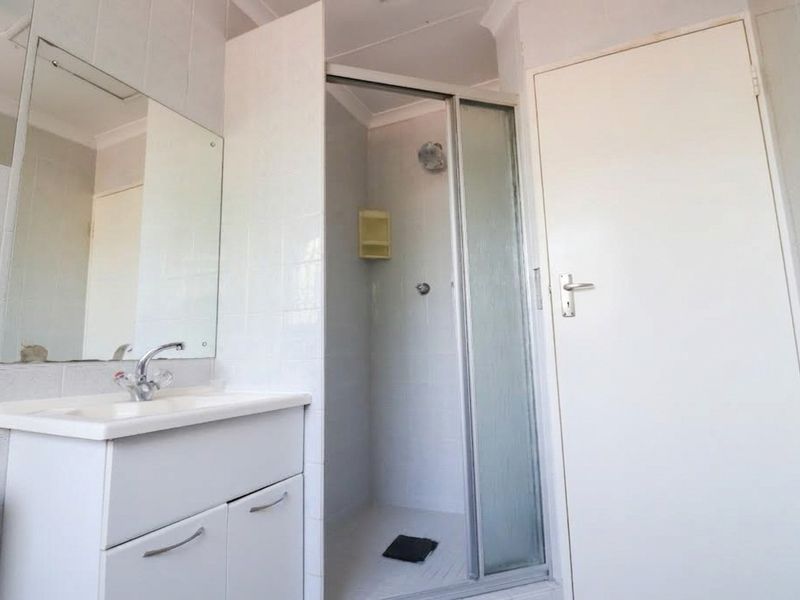 A functional bathroom featuring a white vanity cabinet, basin, wall mirror, and a separate shower enclosure with tiled walls.