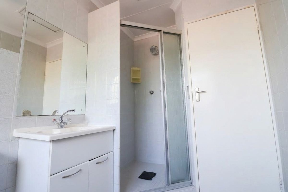 A functional bathroom featuring a white vanity cabinet, basin, wall mirror, and a separate shower enclosure with tiled walls.