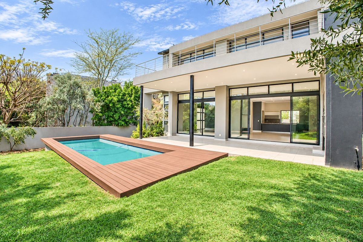 Modern rear exterior featuring a swimming pool with timber decking, a covered patio, and a spacious balcony overlooking the landscaped garden.