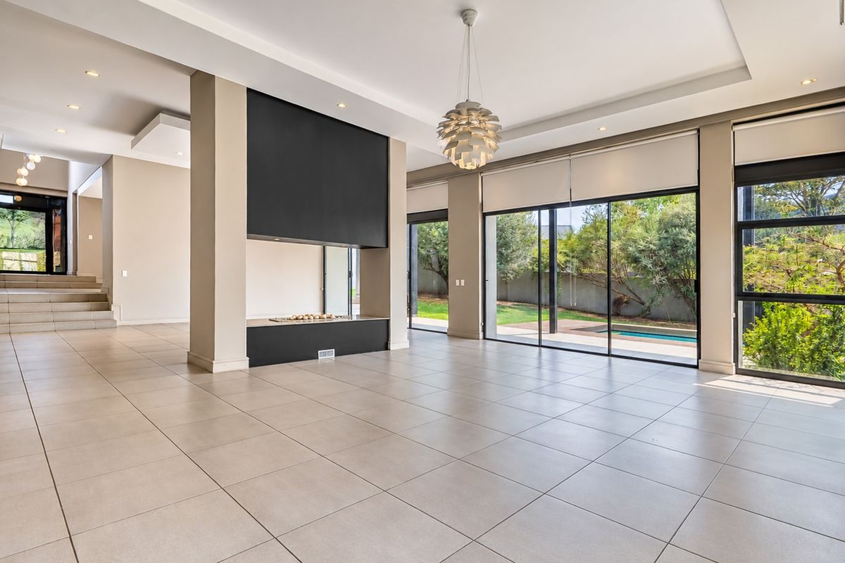 Spacious, light-filled living area featuring large sliding glass doors, modern tiled flooring, a central built-in fireplace, and direct access to the outdoor pool area.