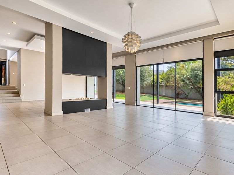 Spacious, light-filled living area featuring large sliding glass doors, modern tiled flooring, a central built-in fireplace, and direct access to the outdoor pool area.
