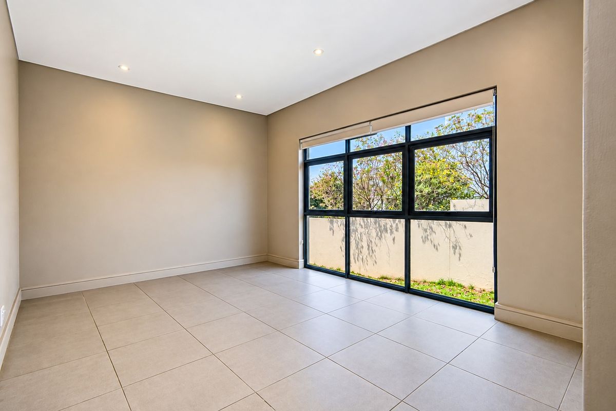 A bright, empty bedroom featuring large aluminium-framed windows, neutral tiled flooring, and recessed downlighting, offering a clean and modern blank canvas.