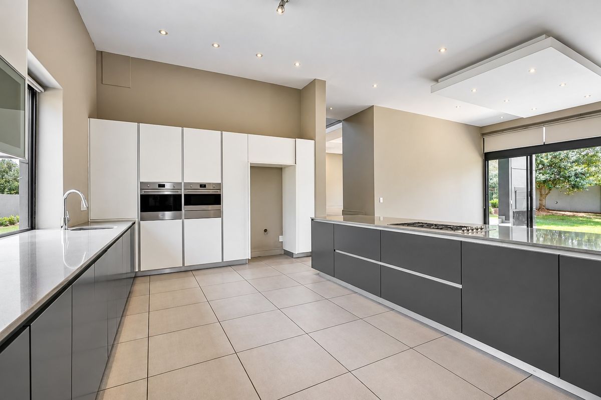 Modern kitchen featuring sleek grey cabinetry, stone countertops, built-in double ovens, a gas cooktop island, and large sliding doors leading to the garden.