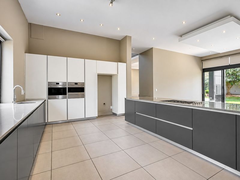 Modern kitchen featuring sleek grey cabinetry, stone countertops, built-in double ovens, a gas cooktop island, and large sliding doors leading to the garden.
