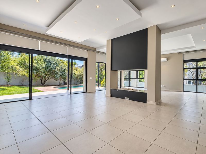 Spacious open-plan living area featuring a modern double-sided fireplace, large sliding glass doors, and recessed ceiling lighting with views of the pool area.