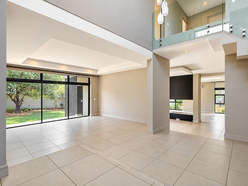 Spacious open-plan living area featuring large sliding glass doors, tiled flooring, a modern glass balustrade staircase, and a built-in fireplace.