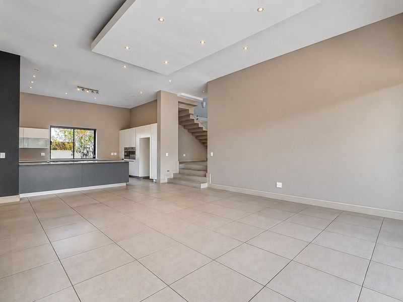 Spacious open-plan living and kitchen area featuring modern tiled flooring, recessed ceiling lighting, and a sleek kitchen island with built-in cabinetry.