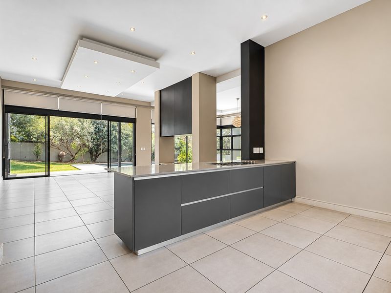 Modern open-plan kitchen featuring a sleek central island with built-in cooktop, tiled flooring, and large sliding doors opening to the garden.