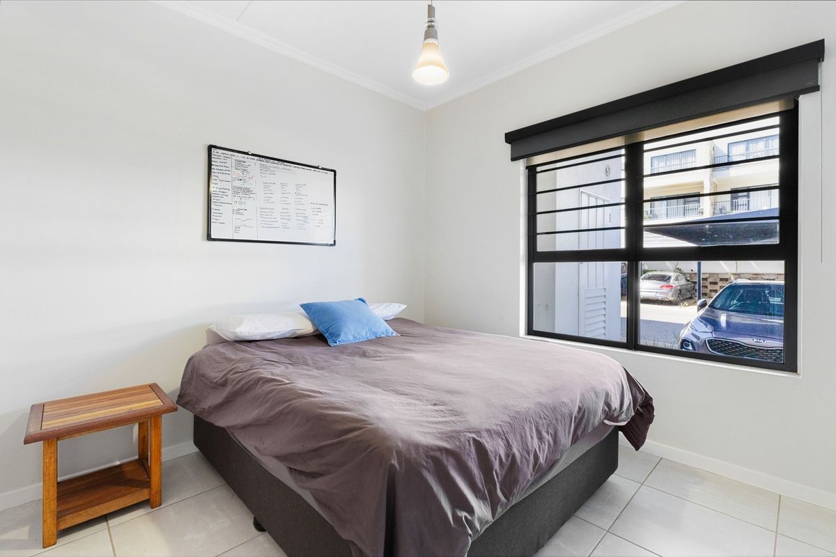 A bright bedroom featuring tiled flooring, a large window with security bars and a roller blind, and a central pendant light fixture.