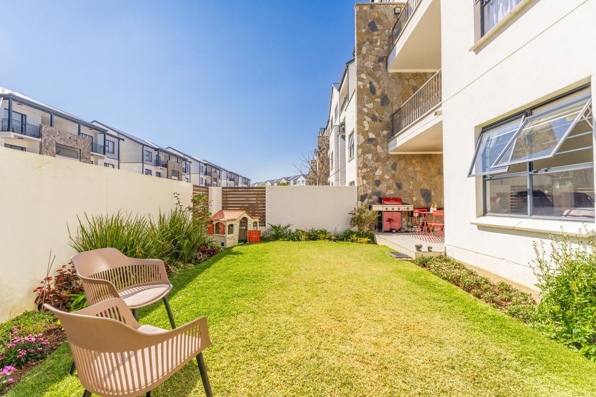 A private rear garden featuring a well-maintained lawn, stone-clad building facade, and a covered patio area.