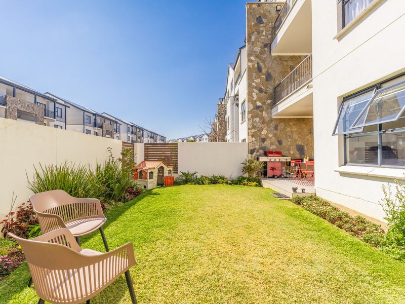 A private rear garden featuring a well-maintained lawn, stone-clad building facade, and a covered patio area.