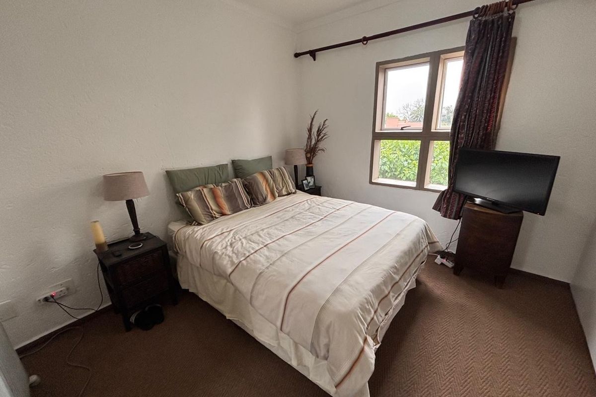 A functional bedroom featuring neutral walls, carpeted flooring, and a window with a curtain rod.