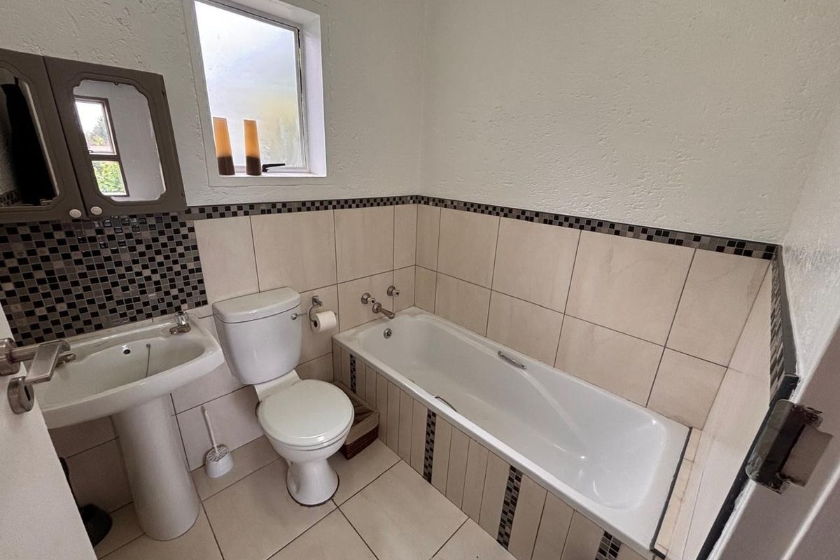 A functional bathroom featuring a pedestal basin, toilet, and bathtub with neutral wall and floor tiling.