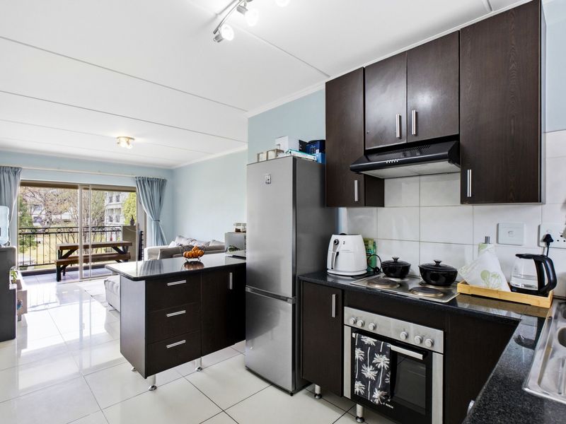 Open-plan kitchen featuring dark wood cabinetry, granite countertops, and built-in appliances, flowing seamlessly into a living area with access to a private balcony.