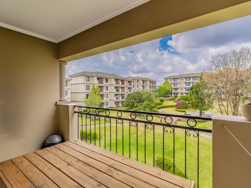 A covered balcony featuring a wrought iron railing, offering pleasant views over the complex gardens and surrounding apartment buildings.