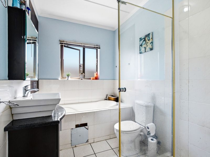 A functional bathroom featuring a built-in bathtub, glass-enclosed shower, vanity basin, and tiled finishes, requiring minor repairs to the bathtub apron.