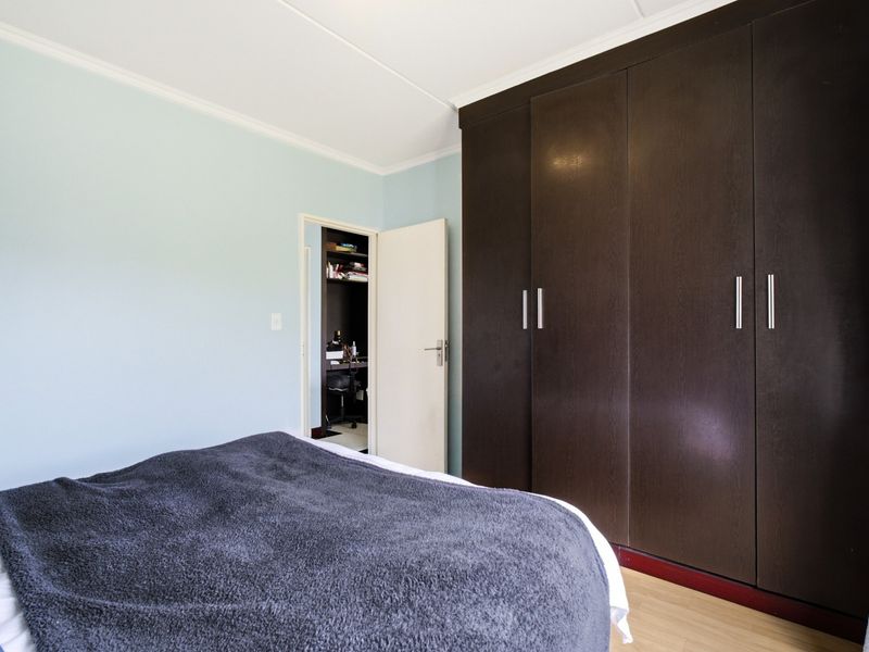 A well-maintained bedroom featuring dark wood built-in wardrobes, light blue walls, and laminate flooring, with an adjacent walk-in closet or storage area.