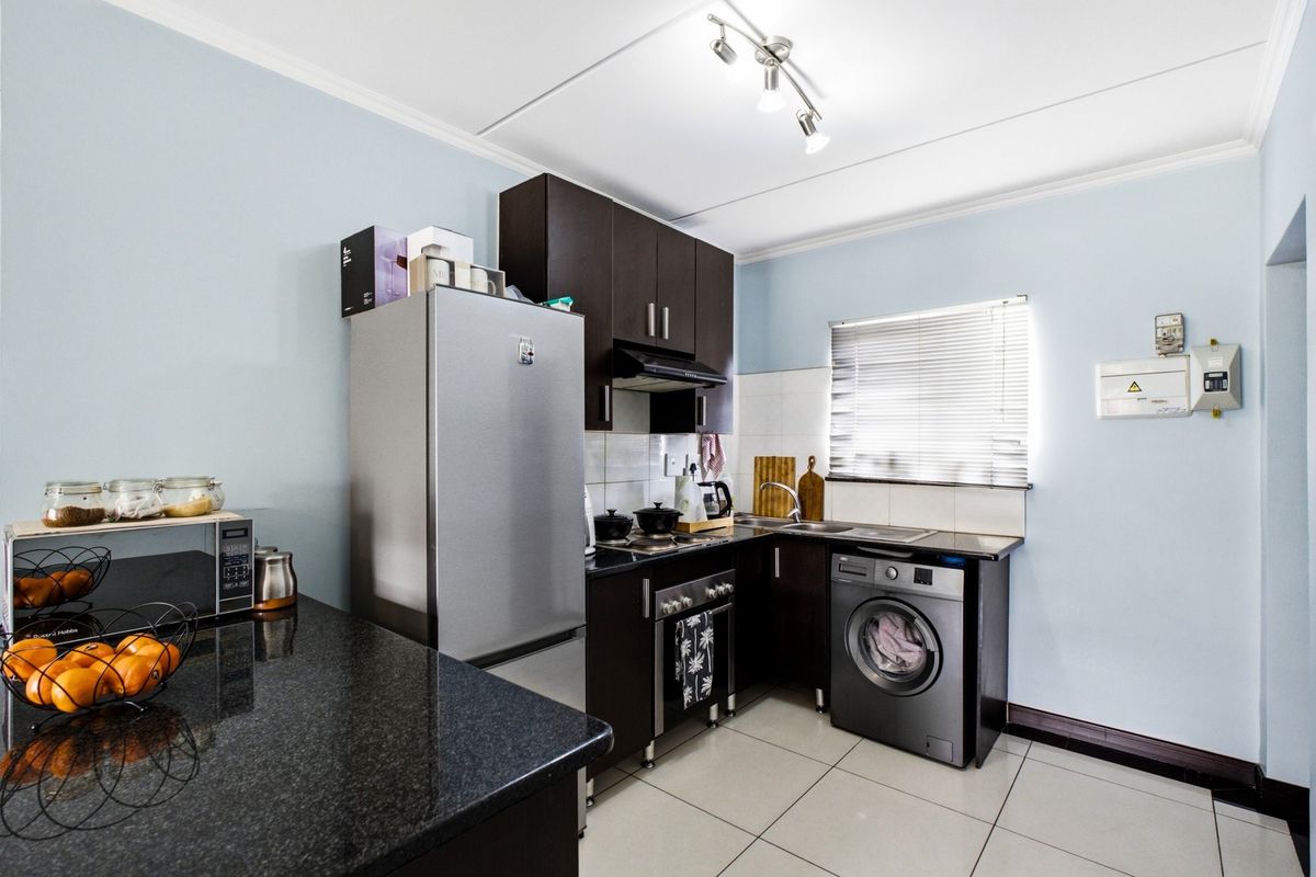 A functional kitchen featuring dark wood cabinetry, granite countertops, tiled flooring, and integrated appliance spaces, providing a clean and practical cooking area.