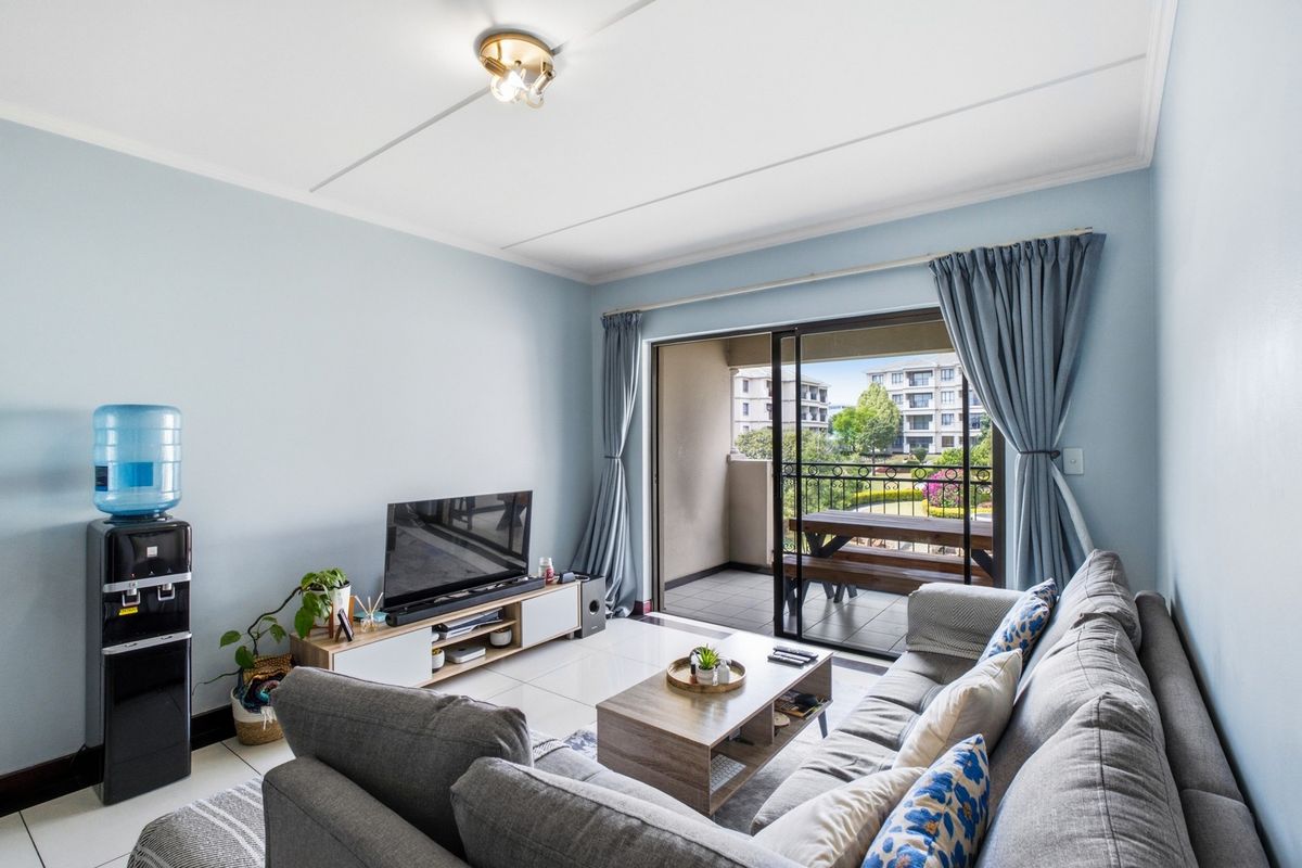 A bright living room featuring tiled floors and a large sliding glass door that opens onto a private balcony with outdoor seating.