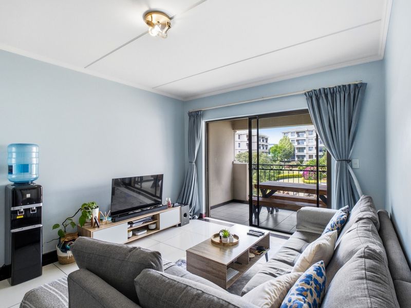 A bright living room featuring tiled floors and a large sliding glass door that opens onto a private balcony with outdoor seating.