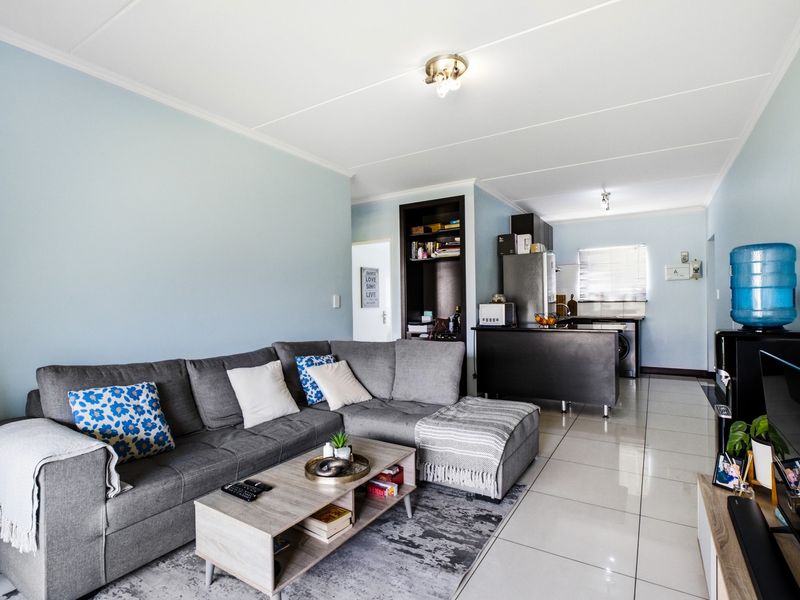 Open-plan living area featuring tiled flooring, a functional kitchen with island, and built-in shelving, creating a cohesive and practical living space.