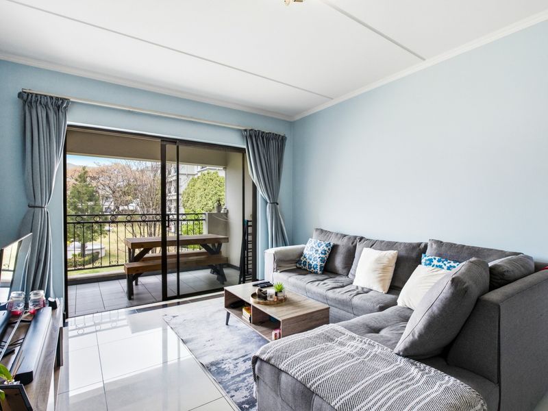 A bright living room featuring large sliding glass doors that open onto a private balcony, complemented by clean tiled flooring.
