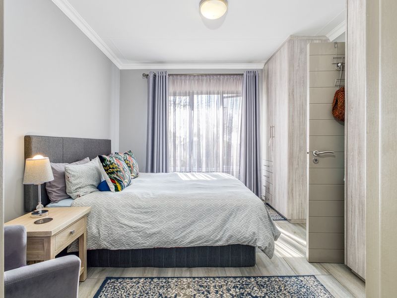 A well-maintained bedroom featuring light-toned laminate flooring, built-in cupboards, and neutral wall finishes, offering a bright and comfortable living space.