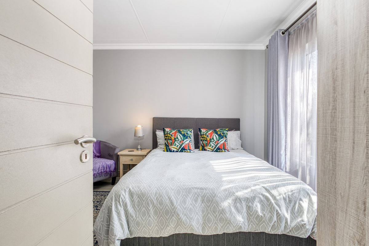 A well-maintained bedroom featuring neutral wall tones, coving, and natural light through a window with fitted curtain rods.
