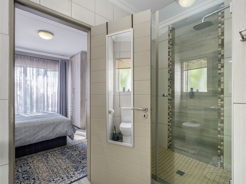 Modern bathroom featuring a glass-enclosed shower with a rain shower head, mosaic tile detailing, and neutral ceramic wall tiles.