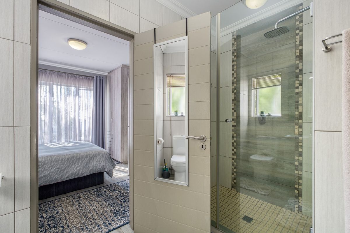 Modern bathroom featuring a glass-enclosed shower with a rain shower head, mosaic tile detailing, and neutral ceramic wall tiles.