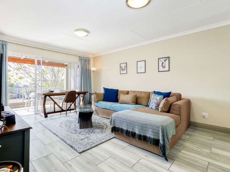A bright living room featuring tiled flooring, coved ceilings, and a large sliding glass door providing access to an outdoor balcony area.
