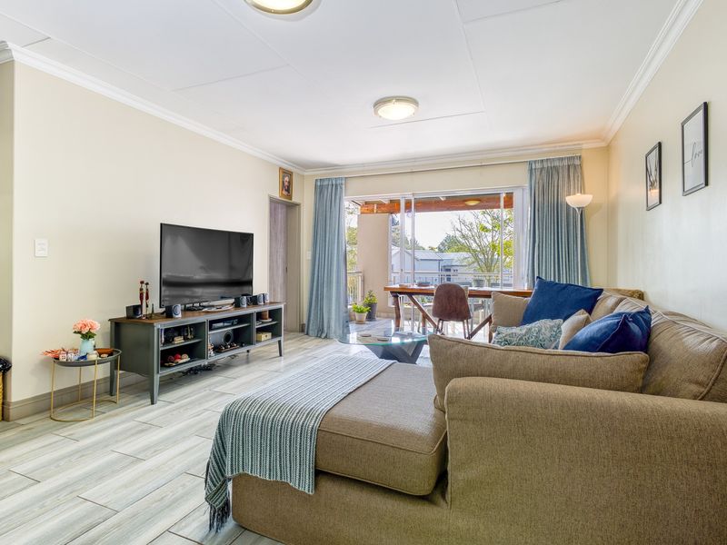 A bright and well-maintained living room featuring tiled flooring, crown molding, and a large sliding glass door providing access to an outdoor balcony area.