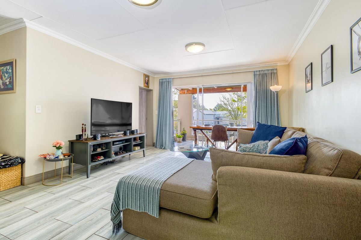 A bright and well-maintained living room featuring tiled flooring, crown molding, and a large sliding glass door providing access to an outdoor balcony area.