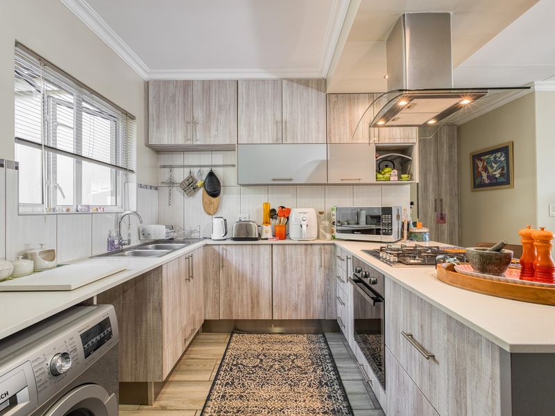 Modern U-shaped kitchen featuring light wood-grain cabinetry, stone countertops, integrated stainless steel appliances, and a gas hob with an overhead extractor fan.