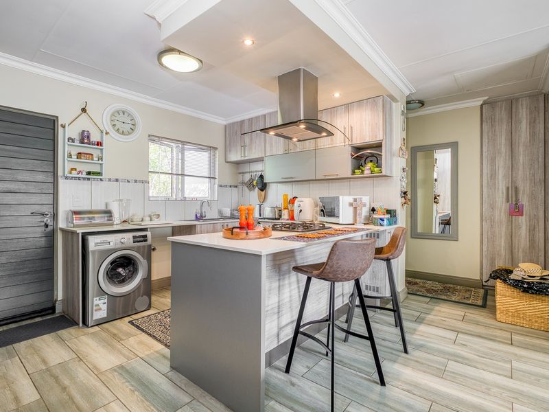 Modern kitchen featuring light wood-grain cabinetry, a central island with breakfast bar, gas hob, extractor fan, and integrated laundry plumbing.