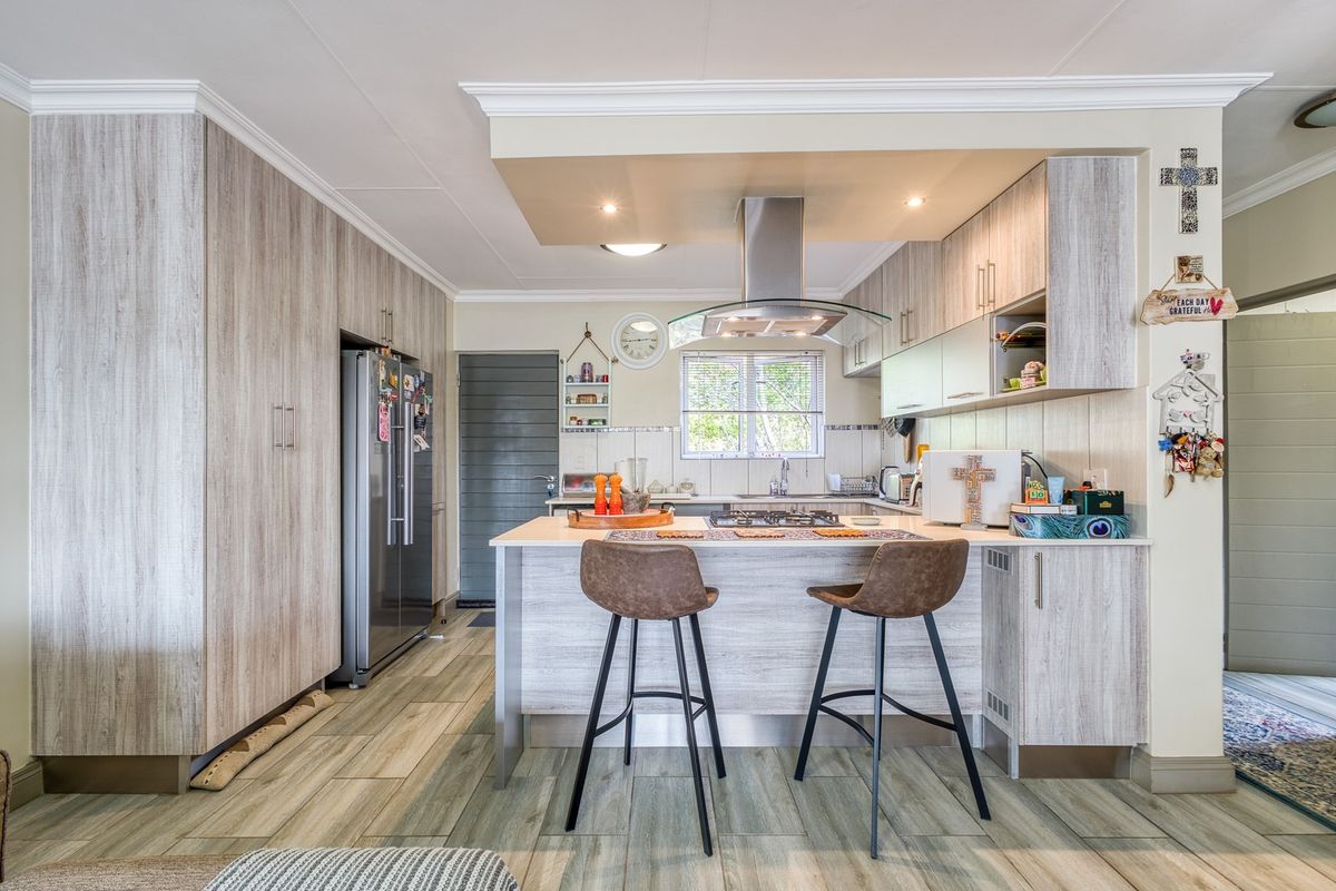 Modern kitchen featuring light wood-grain cabinetry, a central island with a gas hob, extractor fan, and durable tiled flooring.