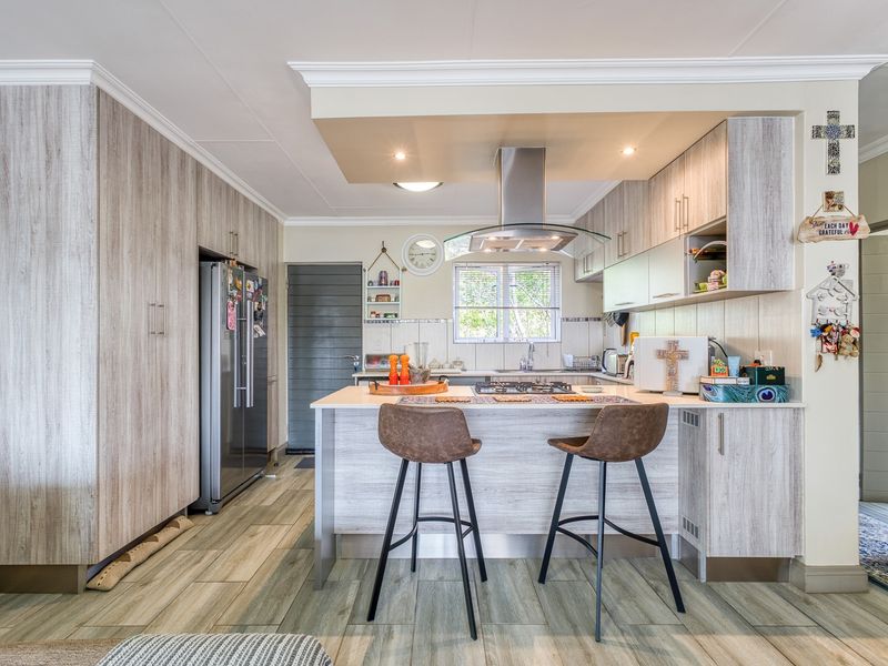 Modern kitchen featuring light wood-grain cabinetry, a central island with a gas hob, extractor fan, and durable tiled flooring.