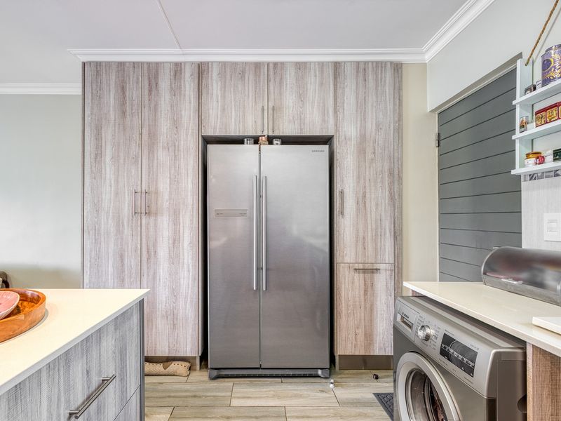 Modern kitchen featuring wood-grain cabinetry, stone countertops, integrated fridge housing, and a built-in washing machine with tiled flooring.
