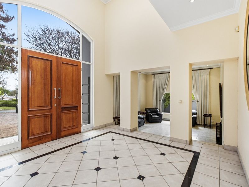 Spacious double-volume entrance hall featuring elegant timber double doors, arched transom window, and classic tiled flooring with decorative inlay.