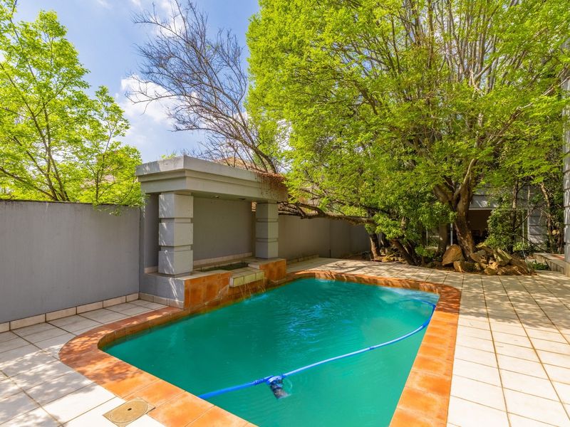 Outdoor pool area featuring a built-in water feature, tiled surround, and mature trees providing shade within a private walled garden setting.