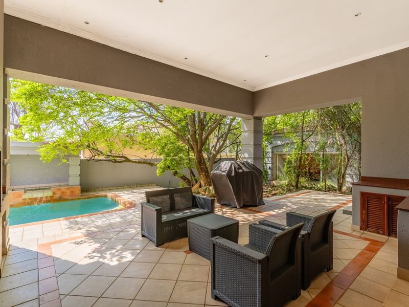 Spacious covered patio featuring a built-in braai, tiled flooring, and direct access to a private swimming pool and garden area.