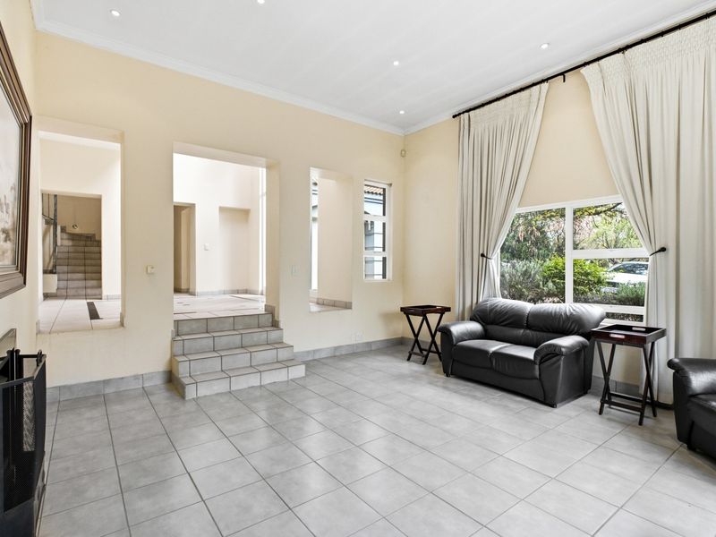 Spacious living room featuring neutral tiled flooring, recessed lighting, a built-in fireplace, and large windows with access to adjacent living areas via tiled steps.